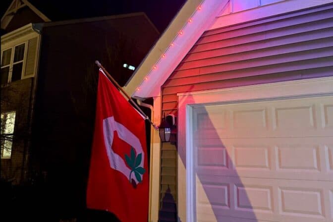 Attached image file A red flag with a white O and a green leaf hangs beside a garage; red and blue lights illuminate the roofline of the house at night.