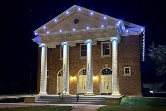 Attached image file A brick building with four large white columns, labeled Kingsford Office, is illuminated by white lights at night. Three arched double doors are visible, and steps lead up to the entrance.